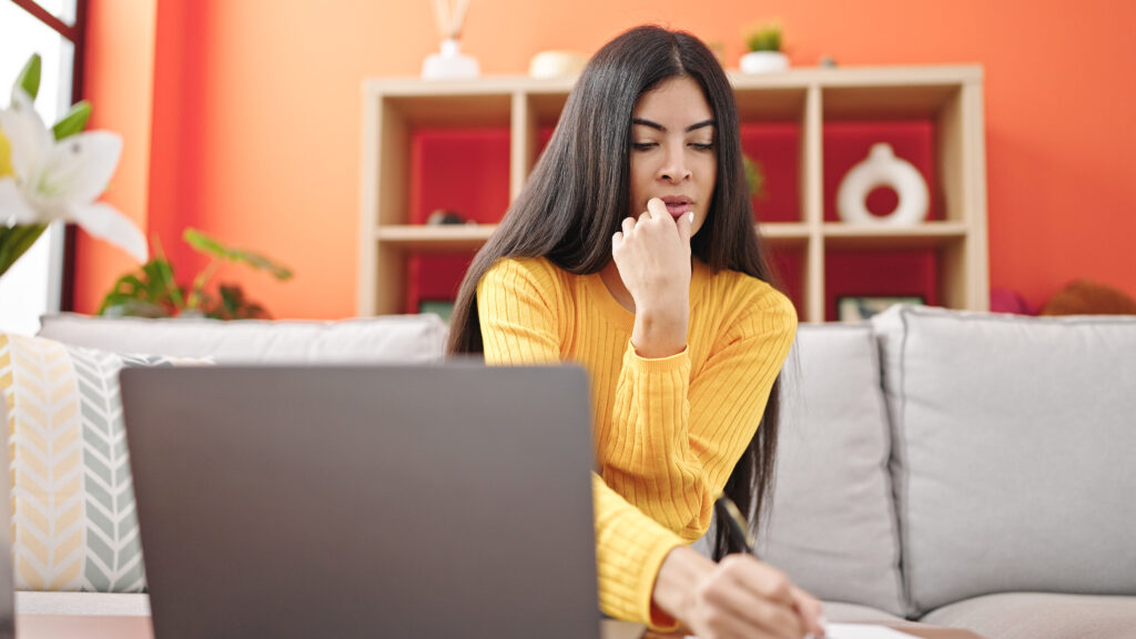 Imagen de Young beautiful hispanic woman using laptop writing on notebook at home