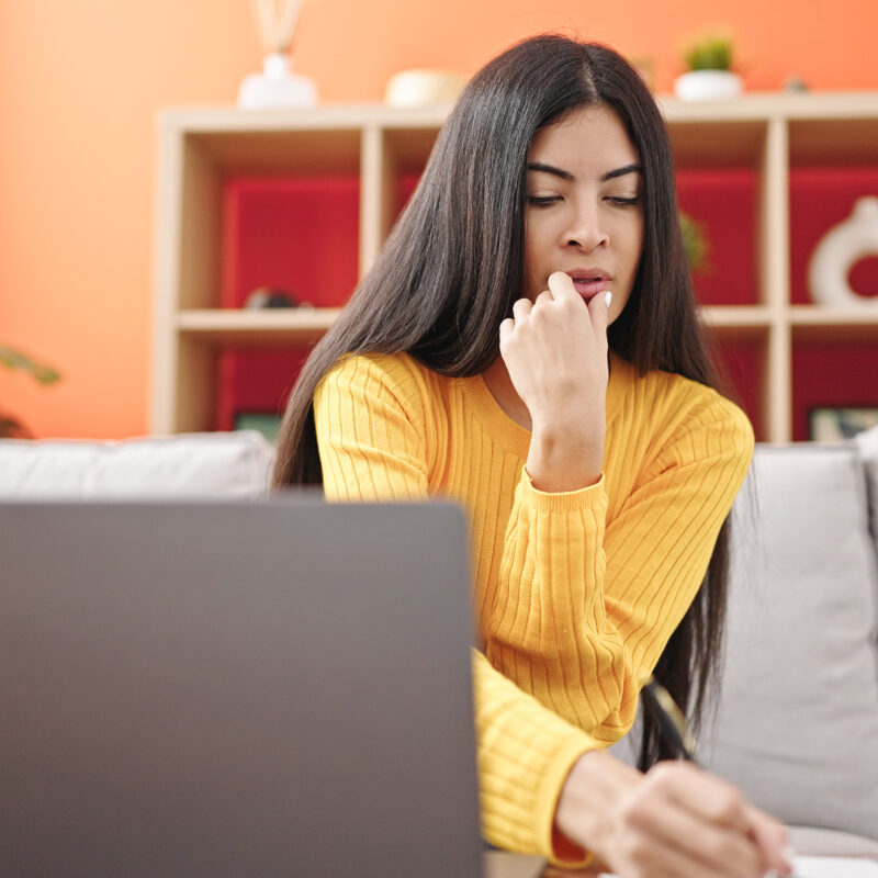 Imagen de Young beautiful hispanic woman using laptop writing on notebook at home