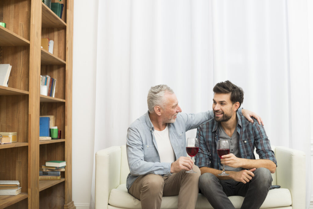 Imagen de Aged man hugging young smiling guy with glasses wine sofa room